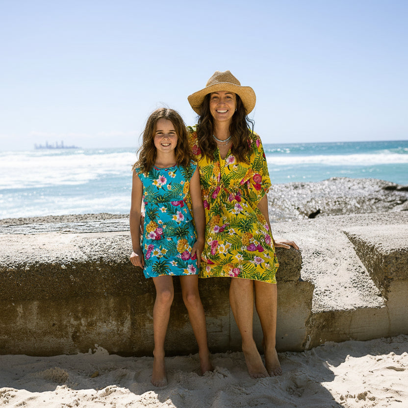 Two women in colorful floral dresses standing on a beach with ocean in the background.