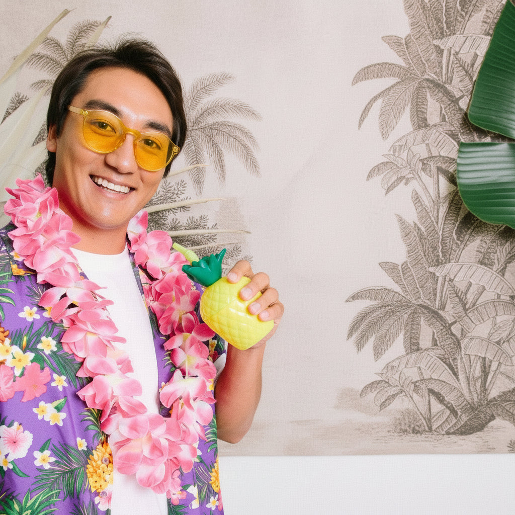 Person wearing a colorful shirt and pink hawaiian flower lei tropical party accessory, holding a pineapple-shaped cup, with a tropical-themed background.