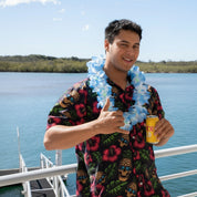 Person wearing a Tropicooll shirt and blue hawaiian flower lei tropical party accessory, holding a beer, with a river in the background.