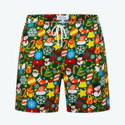 A pair of men's swim trunks by Tommy Hilfiger, featuring a vibrant Christmas-themed all-over print on a dark green background with white drawstrings. The print includes festive icons like snowflakes, Santa Claus, snowmen, Christmas trees, candy canes, ornaments, and gifts in red, yellow, blue, and white.