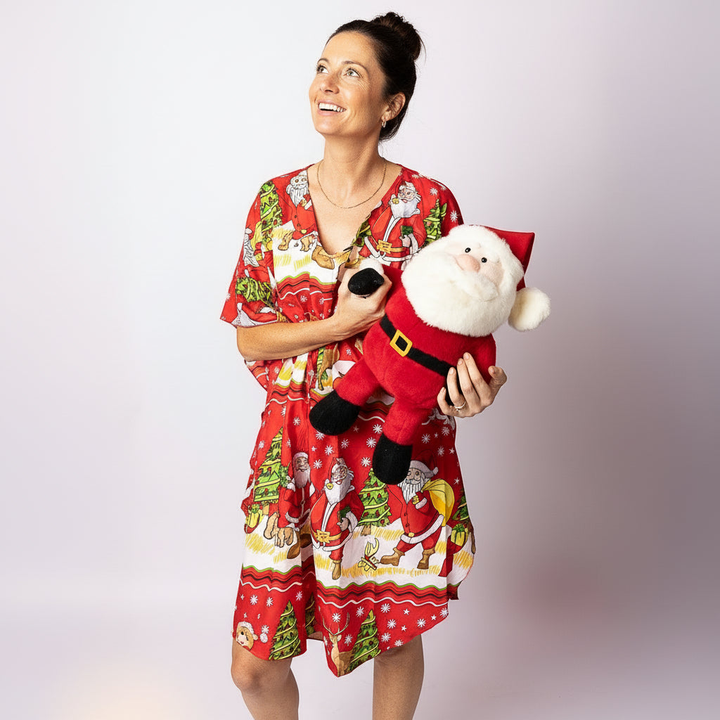 Woman smiling and holding a Santa plush while wearing the Tropicool Happy Santa Red Kaftan. Bright festive print kaftan for Australian Christmas celebrations
