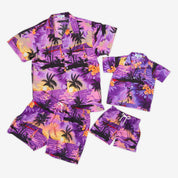 The Sunset Purple Kids Hawaiian Shirt and Shorts Set features vibrant tropical prints in purple, pink, and orange with palm trees—perfect for summer and pictured laid flat on a white background.