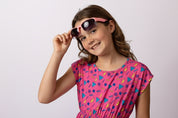 Young girl wearing colorful sunglasses and a patterned dress against a light background