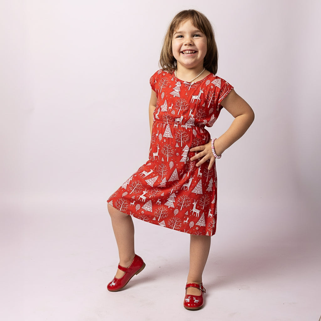 Child wearing the Tropicool Holly Reindeer Red Kids Dress posing playfully with hand on hip, showcasing the Christmas print.